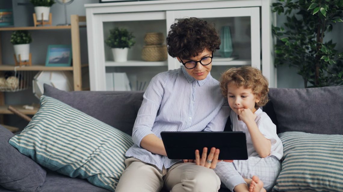 Niño utilizando una tablet mientras un adulto supervisa el uso de pantallas en la infancia